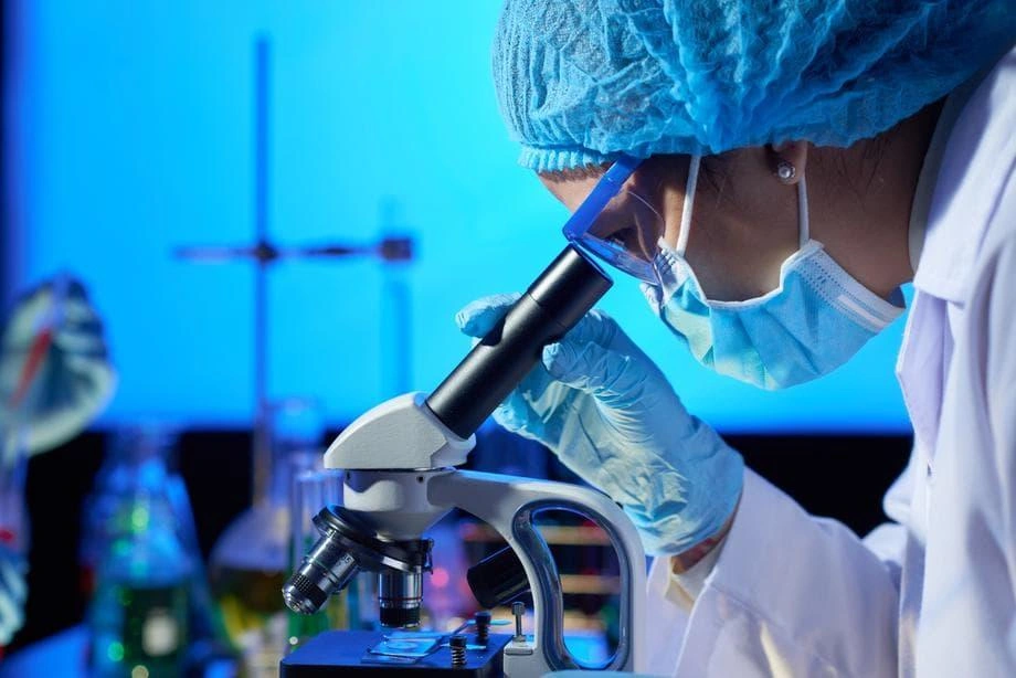 Profissional do laboratório analisando uma amostra ao microscópio na bancada de análises
